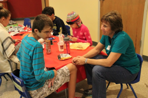 Barb Schmidt talks with and helps one of the special needs kids, Michael Ring, while other children at the table work on making Christmas themed crafts with the assistance of volunteers. All volunteers and children were welcome to help with or attend the Loving Hands program at the First United Methodist Church in Coppell on Dec. 6. Photo by Amanda Hair. 