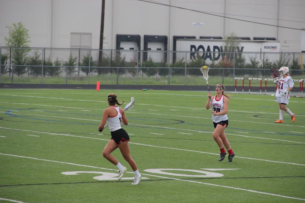 Junior midfield Delaney Dendy prepares to catch the ball from sophomore defense Meghan McAdams Thursday night at the Coppell Middle School West’s field. Cowgirls are advancing to the next round of playoffs which will be on Saturday.  Photo by Aubrie Sisk.