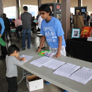Volunteer Nihant Tallapaka helps a child at the Coppell Arts Festival on Oct. 31. “I signed up online two weeks ago and I’ve been looking forward to it,” Tallapaka said. Photo by Ayoung Jo. 
