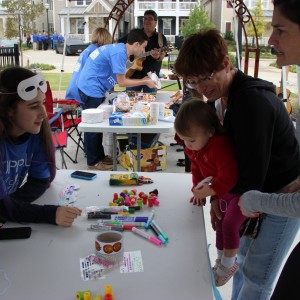 Coppell Middle School North student Sophia Greenberg helps a toddler decorate a mask at the Coppell Arts Festival on Oct. 31. “My mom is an artist and has a booth here,” Greenberg said. “So I signed up with her and brought a friend along.” Photo by Ayoung Jo.