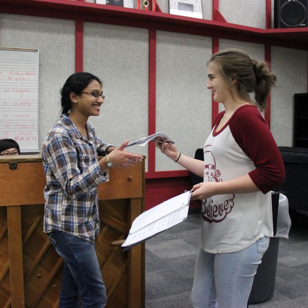 Coppell High School junior Jubi Bijumon is handed a packet of music by sophomore Georgina Bourbon in the Coppell choir room on Dec. 3. Bijumon sings the first alto part in her group. Photo by Jennifer Su.